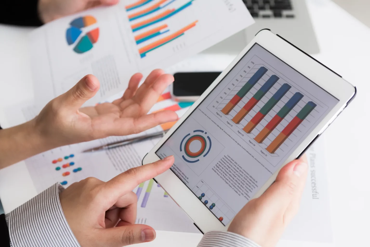 Pessoa analisa métricas e KPIs em um tablet, com gráficos de barras e indicadores na tela, enquanto revisa relatórios impressos de desempenho e indicadores de negócio.