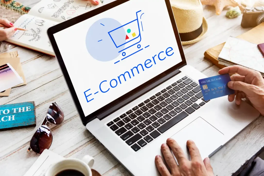 Pessoa usando notebook com tela exibindo E-Commerce e ícone de compras, enquanto segura um cartão na mão; mesa com livros e café, cenário de recuperação de carrinho abandonado.